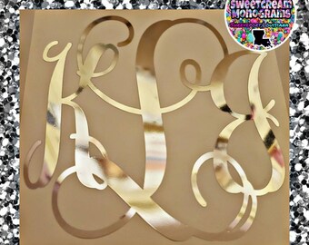 May include: Gold monogram letters K, L, and S in a cursive script font on a beige background. The letters are cut out of gold vinyl and have a reflective finish. The background is a light beige color. The letters are arranged in a traditional monogram style, with the K on top, the L in the middle, and the S on the bottom. The letters are all the same size and are centered on the background. The monogram is a popular choice for personalized gifts and home decor.