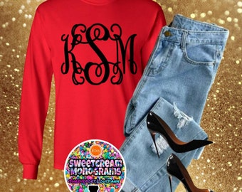 May include: Red long-sleeve shirt with a black monogram of the letters "KSM" in a script font. The shirt is paired with blue jeans and black high heels. A colorful sticker with the text "Sweetcream Monograms Shreveport, Louisiana" is in the lower left corner of the image.