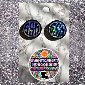 May include: Two black and silver glitter monogram earrings with the letters "SSM" in white. The earrings are on a white marble surface with a round sticker that says "Sweetcream Monograms Shreveport, Louisiana" with a colorful sprinkle design.