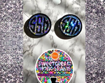 Puede incluir: Dos pendientes de monograma de purpurina negra y plateada con las letras "SSM" en blanco. Los pendientes están sobre una superficie de mármol blanco con una pegatina redonda que dice "Sweetcream Monograms Shreveport, Louisiana" con un diseño de chispas de colores.