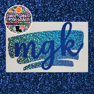 May include: A blue glitter background with a white rectangle containing a blue brush stroke with the letters "mgk" in blue.