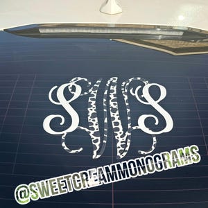 May include: A white monogram decal with the letters SWS, with the middle letter featuring a black and white cow print design. The decal is affixed to a car window. The text "@SWEETCREAMMONOGRAMS" is at the bottom.