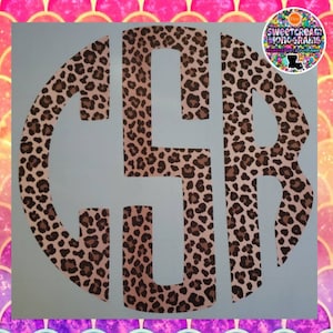 May include: A circular monogram decal featuring the letters G, S, and R in a bold, block-style font. The letters are filled with a brown and black leopard print pattern against a light background. A small circular logo is visible in the top right corner.