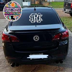 May include: A black car with a white monogram sticker on the back window. The monogram is "J.R.K." The car also has a Mercedes-Benz emblem on the back.