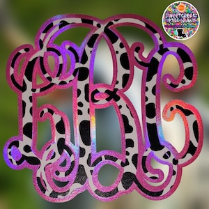 May include: A pink and black cow print monogram with a holographic finish. The monogram is in the shape of the letters "KR".