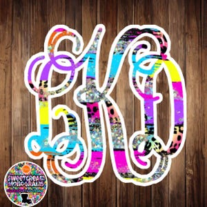 May include: A colorful monogram letter K with a glittery, striped, and animal print design. The letter is outlined in white and set against a woodgrain background.