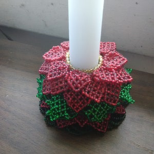 May include: A beaded candle holder with a red poinsettia design and green leaves. The holder is made of small beads and has a gold trim around the top.