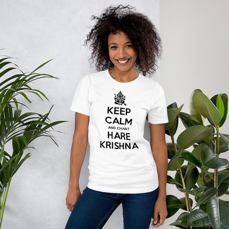 May include: White t-shirt with black text that reads "Keep Calm and Chant Hare Krishna". The text is centered on the shirt and is surrounded by a black outline. A small image of a Hindu deity is above the text.