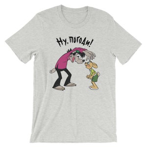 May include: A grey t-shirt with a cartoon wolf and rabbit. The wolf is saying "Ну, погоди!" in Russian.