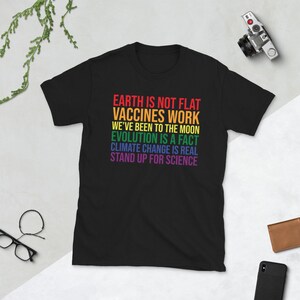 May include: Black t-shirt with a rainbow-colored graphic that reads "EARTH IS NOT FLAT, VACCINES WORK, WE'VE BEEN TO THE MOON, EVOLUTION IS A FACT, CLIMATE CHANGE IS REAL, STAND UP FOR SCIENCE."