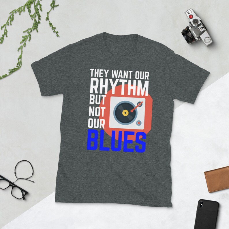 May include: A dark heather grey t-shirt with a white graphic print that says "They want our rhythm but not our blues". The graphic also includes a red circle with a black record player inside.