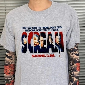 May include: A gray t-shirt featuring the movie title "Scream" in red and blue, with the film's cast. The shirt also has the text "DON'T ANSWER THE PHONE. DON'T OPEN THE DOOR. DON'T TRY TO ESCAPE."