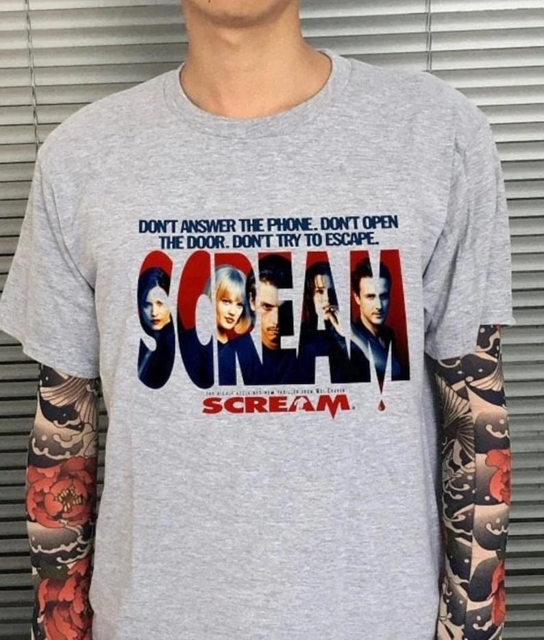 May include: A gray t-shirt featuring the movie title "Scream" in red and blue, with the film's cast. The shirt also has the text "DON'T ANSWER THE PHONE. DON'T OPEN THE DOOR. DON'T TRY TO ESCAPE."