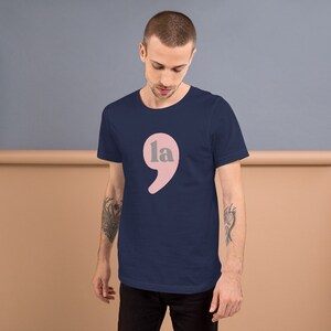 Puede incluir: Una camiseta azul marino con un punto y coma rosa con la palabra "la" en su interior.