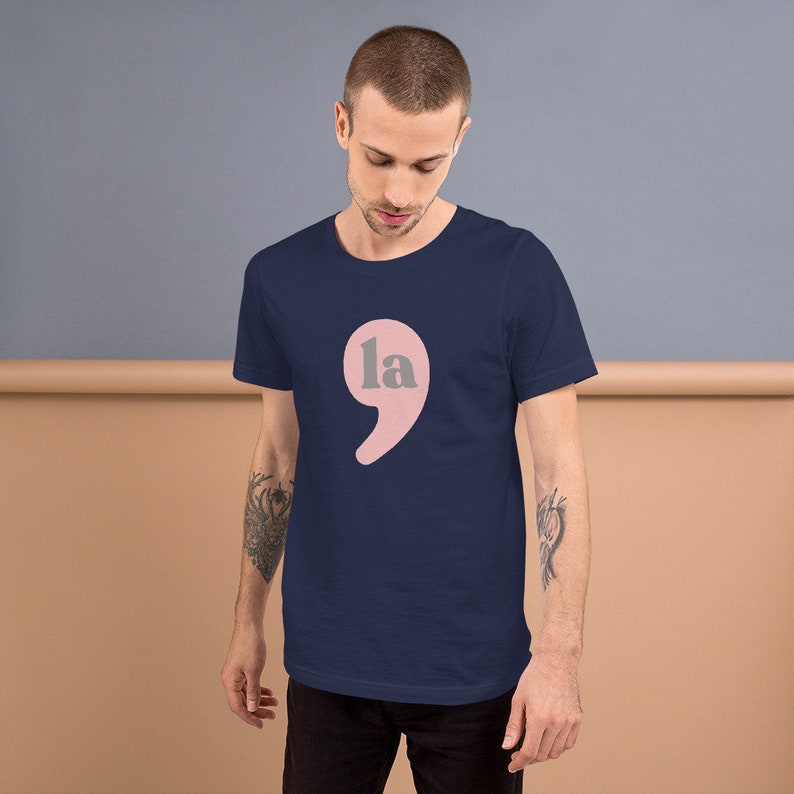 Puede incluir: Una camiseta azul marino con un punto y coma rosa con la palabra "la" en su interior.