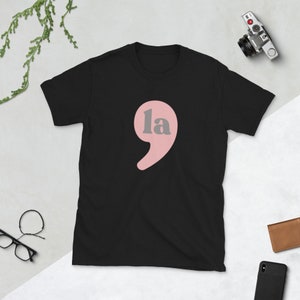 Puede incluir: Camiseta negra con una coma rosa y la palabra "la" en letras grises.