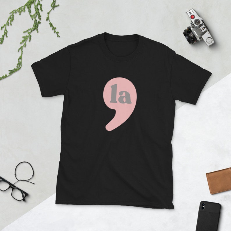 Puede incluir: Camiseta negra con una coma rosa y la palabra "la" en letras grises.