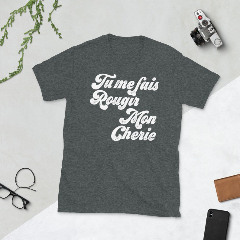 May include: A dark heather grey t-shirt with the text "Tu me fais rougir Mon Cherie" in a white retro font.