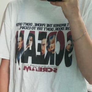 May include: White t-shirt featuring the word "SCREAM" in large, red letters with a movie poster design. The shirt also has the text "DON'T ANSWER THE PHONE. DON'T OPEN THE DOOR. DON'T TRY TO ESCAPE."