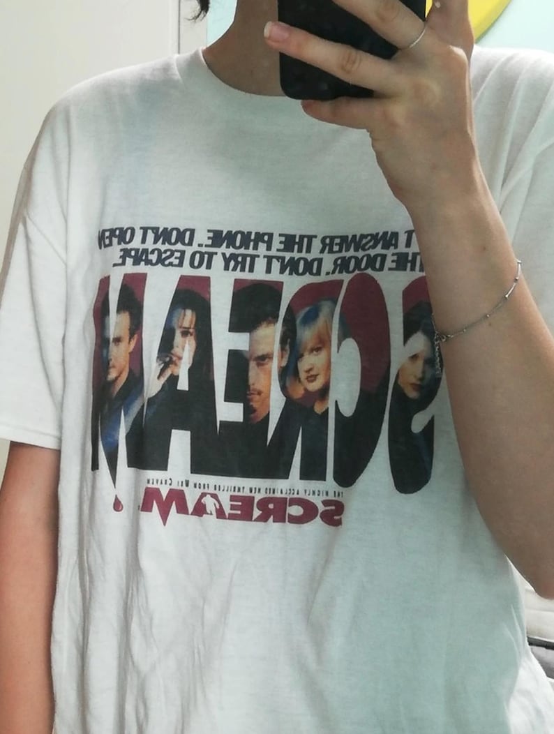 May include: White t-shirt featuring the word "SCREAM" in large, red letters with a movie poster design. The shirt also has the text "DON'T ANSWER THE PHONE. DON'T OPEN THE DOOR. DON'T TRY TO ESCAPE."