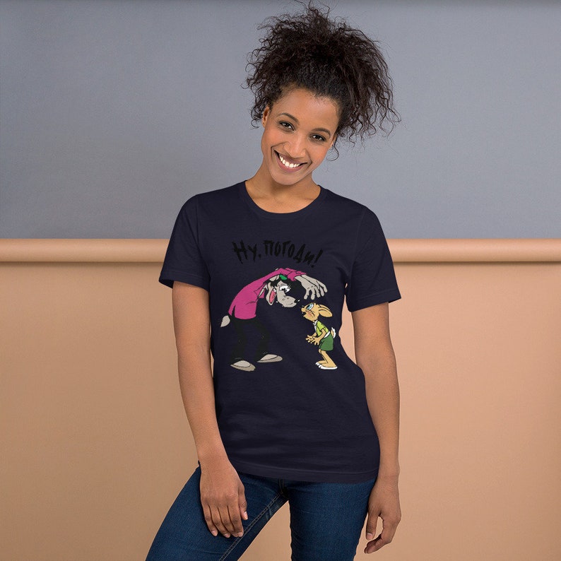 May include: A navy blue t-shirt with a cartoon image of a wolf and a rabbit. The wolf is wearing a pink shirt and the rabbit is wearing a green shirt. The text "Ну, погоди!" is printed on the shirt.