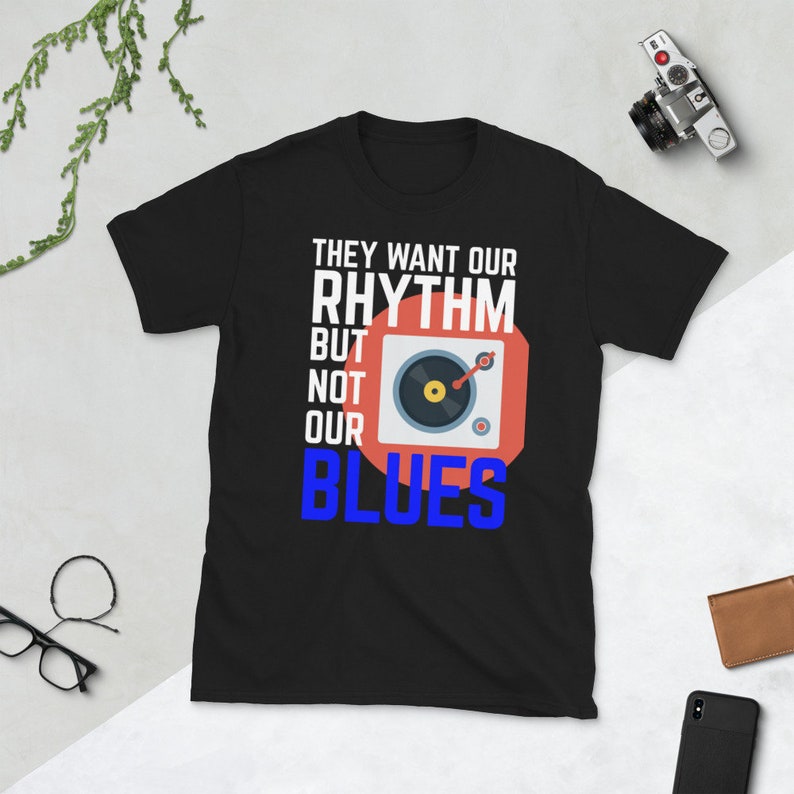 May include: Black t-shirt with white text that reads "They want our rhythm but not our blues". A red circle with a white record player inside is next to the text.