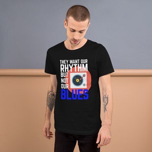 May include: Black t-shirt with a white graphic design that says "They want our rhythm but not our blues". The graphic also includes a red circle with a stylized image of a record player.