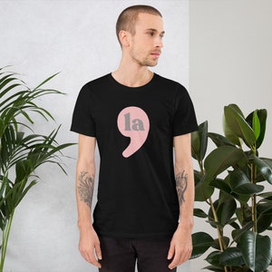 Puede incluir: Una camiseta negra con un punto y coma rosa y el texto "la" dentro del punto y coma.