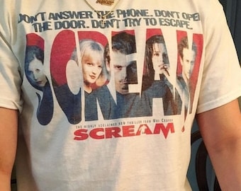 Peut inclure: T-shirt crème avec le mot "SCREAM" en rouge et bleu, et des images de personnages du film. Le t-shirt porte également le texte "DON'T ANSWER THE PHONE. DON'T OPEN THE DOOR. DON'T TRY TO ESCAPE."