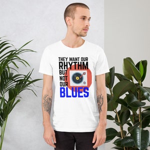 May include: White t-shirt with black text that reads "They want our rhythm but not our blues". A red circle with a black record player inside is next to the text.