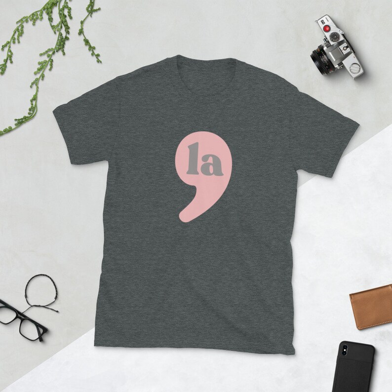 Puede incluir: Una camiseta gris oscuro jaspeada con un signo de puntuaci&oacute;n rosa y la palabra "la" en gris.