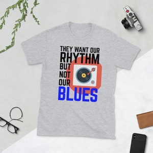 May include: Gray t-shirt with the text "They want our rhythm but not our blues" in black and a red square with a black record player graphic.