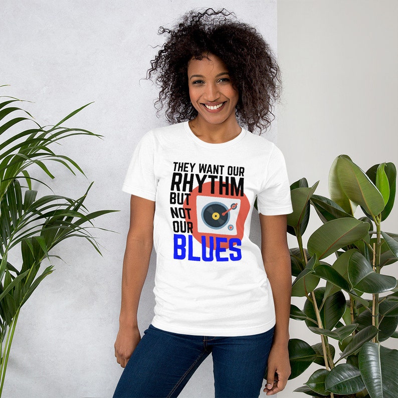May include: White t-shirt with a black and red graphic of a record player and the text "They want our rhythm but not our blues".