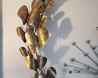 May include: A gold metal wall sculpture with a cascading design of leaves. The leaves are textured and have a slightly iridescent finish.