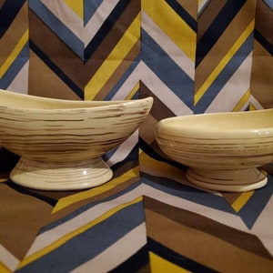 Pode incluir: Duas tigelas de cerâmica com um design listrado marrom e creme. As tigelas estão sobre um fundo estampado marrom e amarelo.