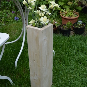 May include: A tall, wooden planter with a square opening, filled with white carnations. The planter is sitting on a green lawn.