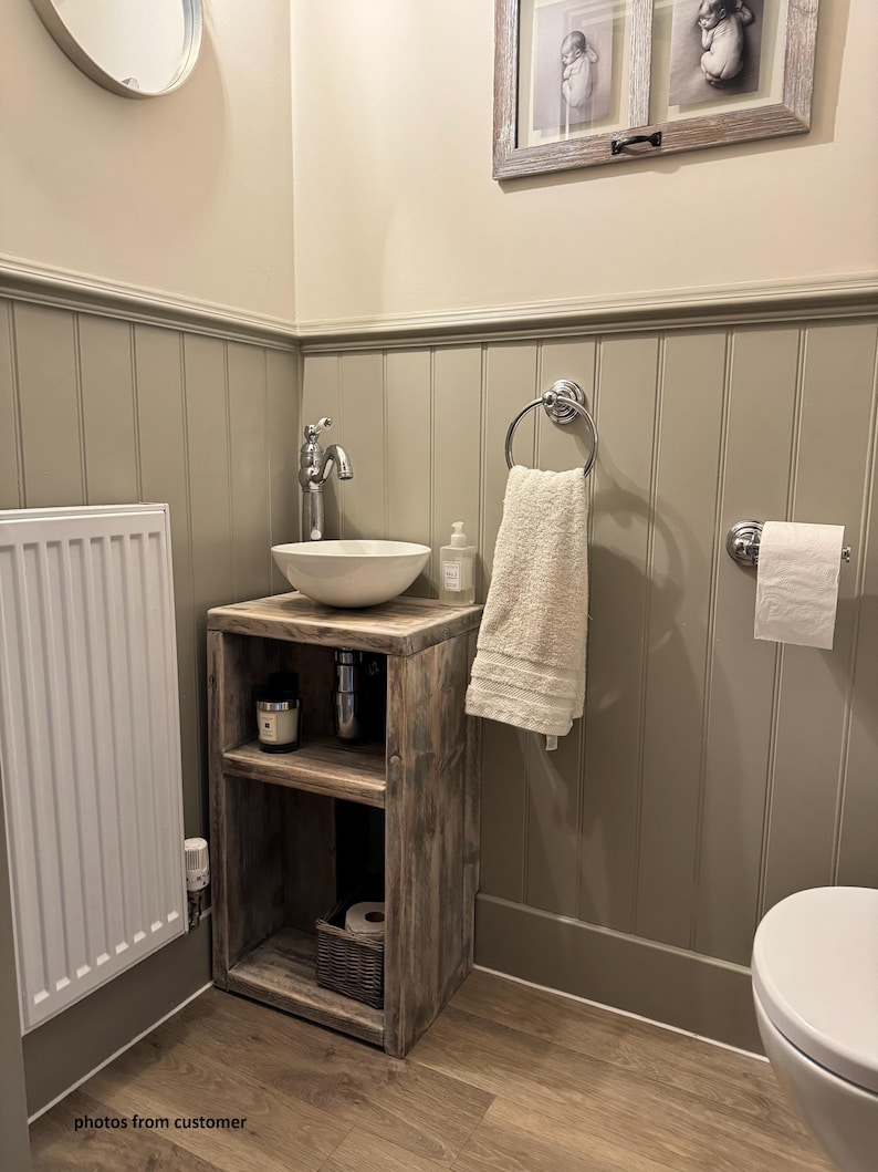 May include: A rustic wooden vanity with a white ceramic sink and chrome faucet. The vanity has open shelving and a woven basket. A white towel hangs on a chrome ring, and a roll of toilet paper is mounted on the wall. The bathroom has a neutral color scheme.