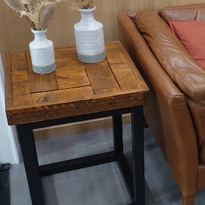 May include: A wooden side table with a black metal frame. The table has a rustic, reclaimed wood top and is decorated with two white ceramic vases with dried flowers.