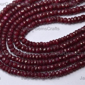 May include: A strand of deep red ruby beads, each bead is faceted and has a slightly irregular shape. The beads are strung together on a clear thread and are arranged in a loose coil.