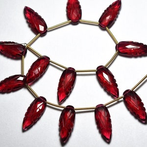 May include: A strand of red gemstone beads, each carved in the shape of a leaf, strung on a gold wire.