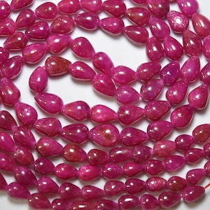 May include: A strand of pink gemstone beads in a teardrop shape. The beads are strung on a clear thread and are arranged in a circular pattern.
