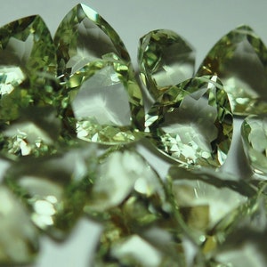 Puede incluir: Un grupo de 20 piedras preciosas verdes facetadas, talladas en forma triangular. Las piedras son translúcidas y tienen un color verde claro.