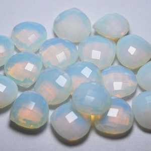 May include: A collection of faceted, opalescent gemstones. The stones are a soft white with subtle hints of yellow and blue, and are cut with multiple facets to catch the light. These gemstones are ideal for jewelry making.