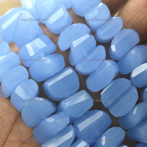 May include: A strand of light blue gemstone beads, each bead is faceted and has a slightly irregular shape. The beads are strung together on a clear thread.