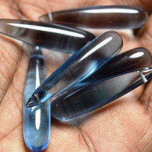May include: A collection of six blue topaz gemstone points, each with a smooth, polished finish. The points are arranged in a hand, showcasing their unique shape and colour.