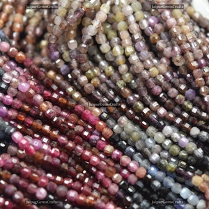 Puede incluir: Primer plano de una variedad de cuentas de piedras preciosas facetadas en tonos azules, rosas y morados. Las cuentas están enhebradas en un hilo blanco fino y están dispuestas en filas. Las cuentas son todas aproximadamente del mismo tamaño y forma, y tienen un acabado liso y pulido.