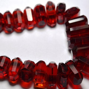 May include: A strand of deep red faceted glass beads, each bead is shaped like a long, narrow rectangle with rounded edges.