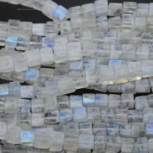 May include: Strands of square-cut, translucent moonstone beads. The beads have a subtle, iridescent sheen with flashes of blue and white. The beads are strung together, creating a textured, natural look, perfect for jewelry making.