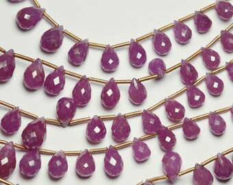 May include: Close-up of several strands of faceted, teardrop-shaped, pink gemstones strung on gold-coloured wire. The gemstones have a sparkling, polished appearance, and are arranged in parallel rows against a white background. These beads are suitable for jewelry making.