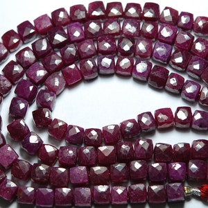 Może przedstawiać: Szereg koralików rubinowych, każdy koralik jest fasetowany i ma kwadratowy kształt. Koraliki są ciemnoczerwone i mają delikatny połysk.